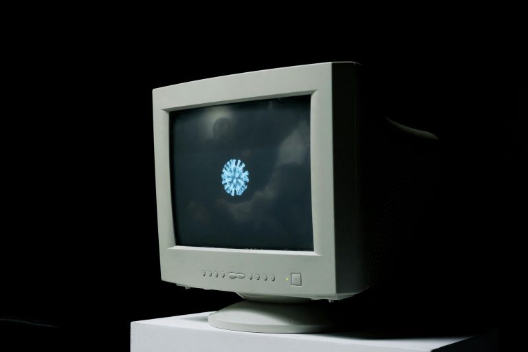 A vintage computer monitor shows an image of a coronavirus on screen against a dark background.